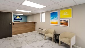 A reception area with a wooden reception desk, a 'Days Inn' sign, two beige chairs, a small table, and framed pictures on the wall. - Days Inn by Wyndham Farmington NM (Farmington)