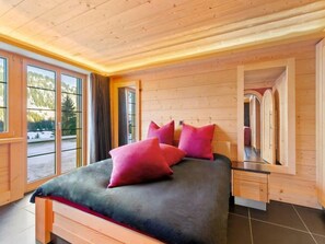 A wooden bedroom with a bed, nightstands, and large windows.