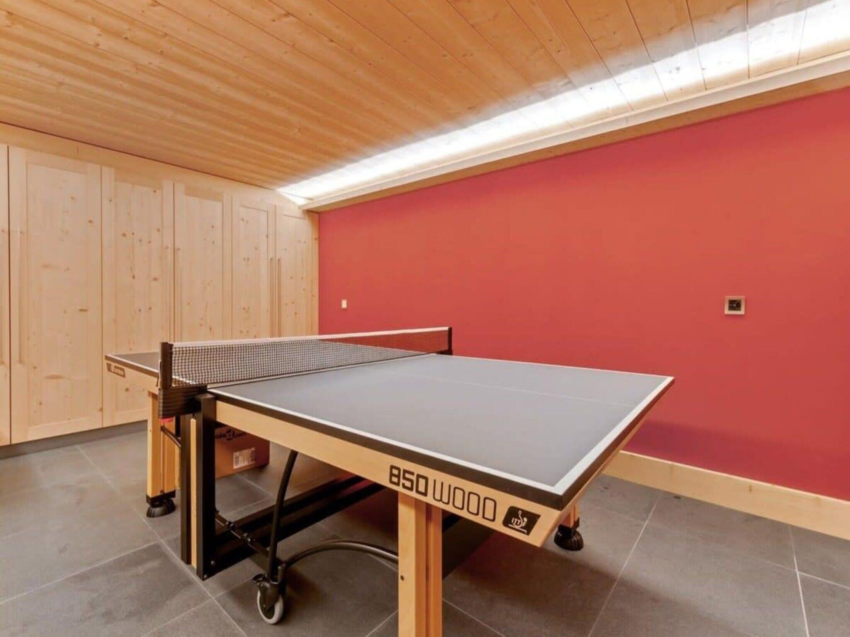 A ping pong table with wheels in a room with wooden walls and a red accent wall.