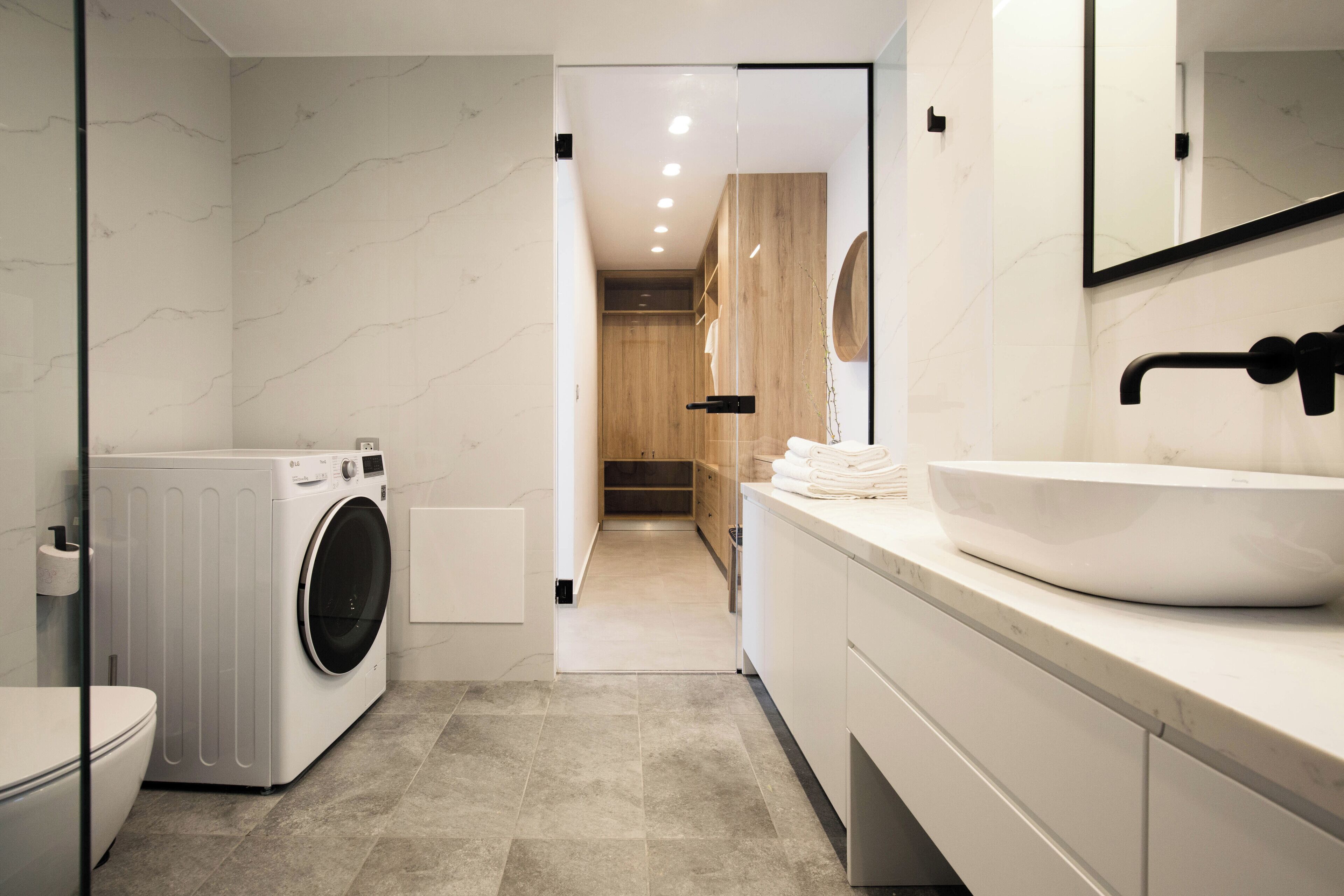 Une salle de bain moderne équipée d’un lave-linge, d’un évier et d’un miroir.