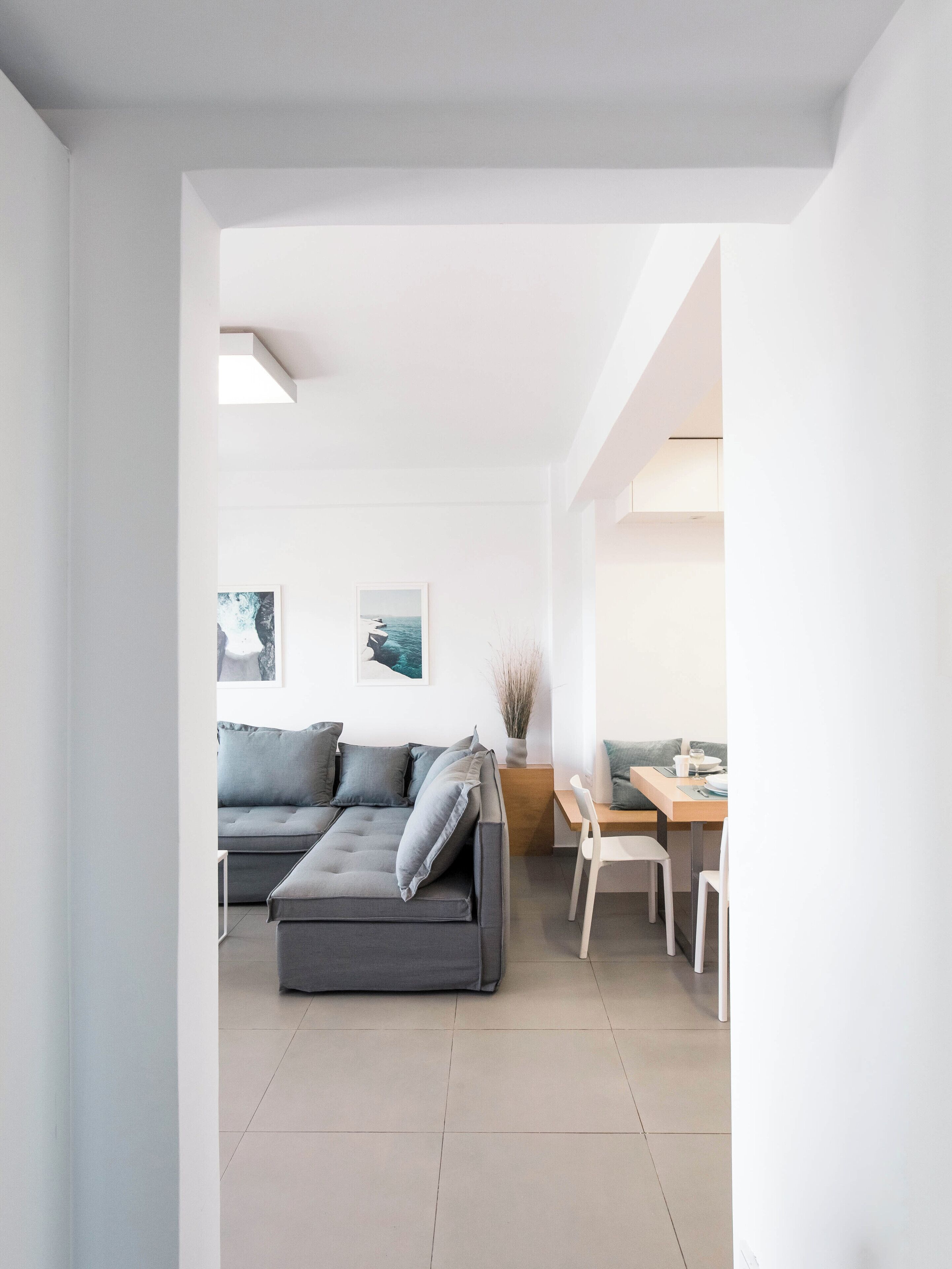 A modern living room with a grey sectional sofa, a dining area with a wooden table and chairs, and artwork on the walls.