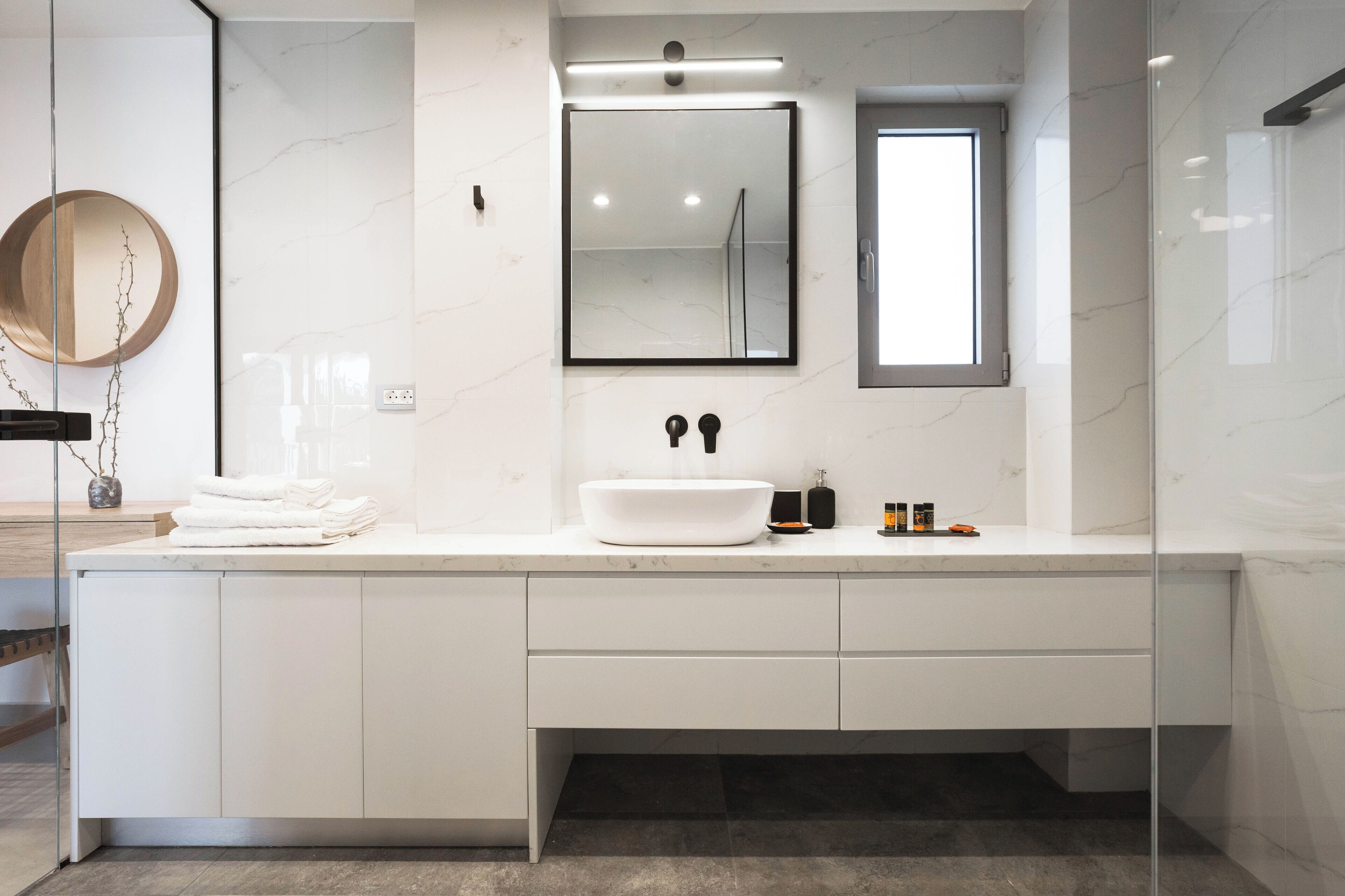 A modern bathroom with a large white sink, a round mirror, and a glass shower enclosure.