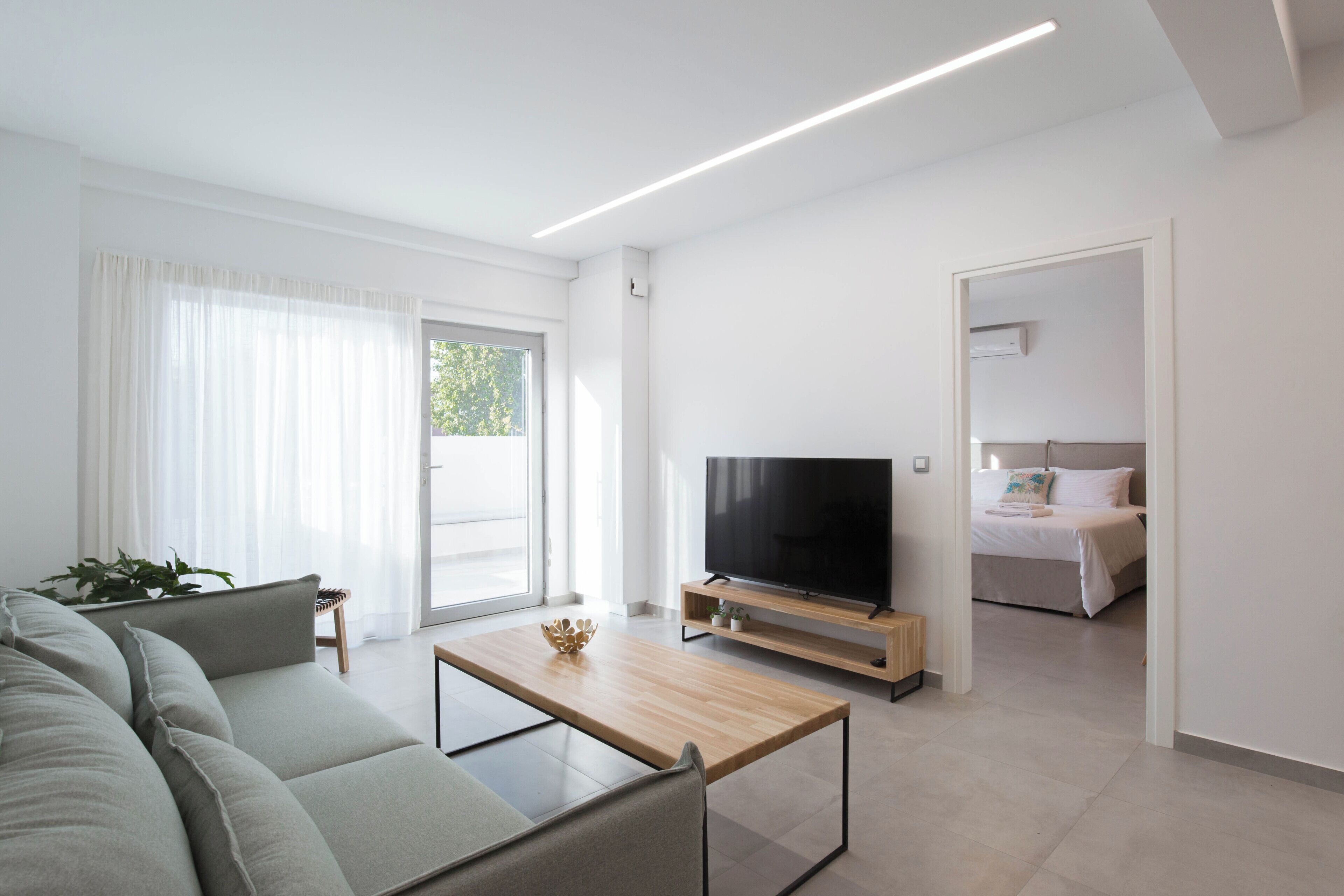 A modern living room with a sofa, a coffee table, a TV, and a bed in the background.