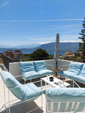 A terrace with blue cushioned chairs and a table, overlooking a mountainous landscape with a clear sky. - Hermes & Dione (Chania)