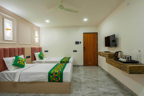 Habitación de hotel con dos camas, televisor, una encimera de madera con cafetera y ventilador de techo.