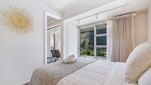 A hotel room with a large bed, a view of a mountainous landscape through a window, and a modern decor including a wall art piece. - Luxury Interiors in Prime Location (Queenstown)