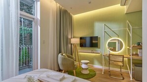 Quarto de hotel com cama, escrivaninha com luminária, cadeira, televisão e banheiro.