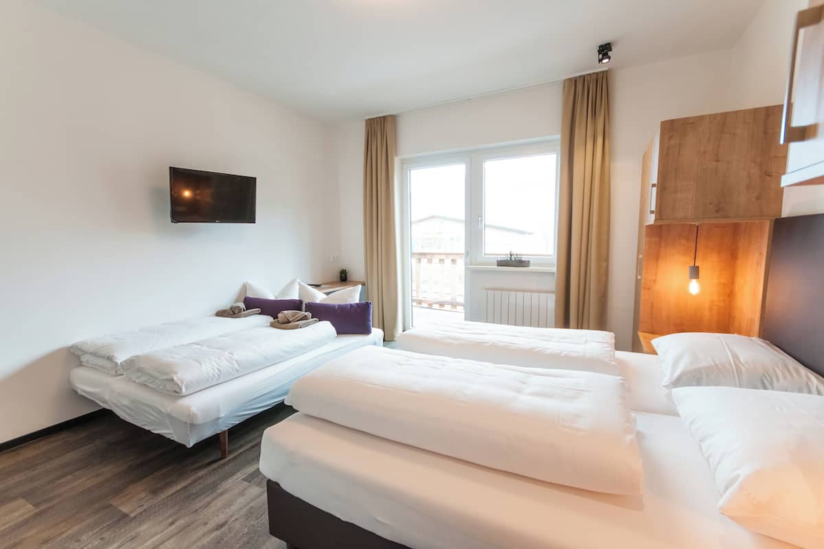 A hotel room with two beds, a flat-screen TV mounted on the wall, a window with curtains, and a wooden headboard.