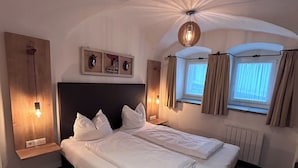 Een tweepersoonsbed in een kamer met een schuine plafond, een houten hoofdbord en een klein raam met gordijnen.