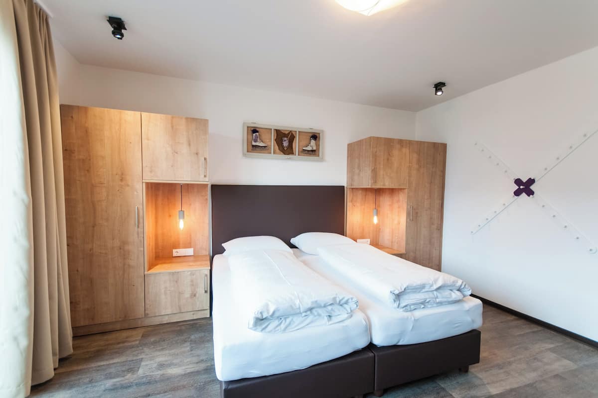 A hotel room with two beds, wooden wardrobes, a wall-mounted light fixture, and a decorative wall piece.