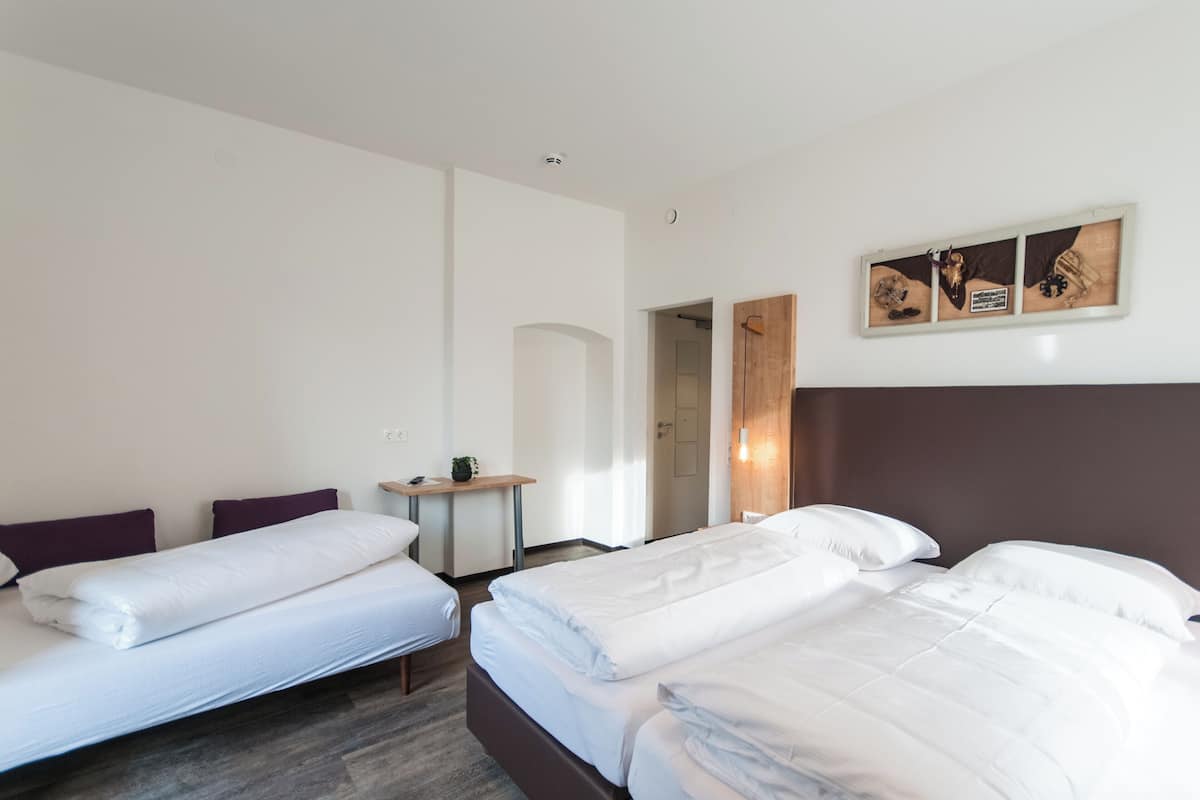 A hotel room with two beds, a small table, and a door leading to another room.