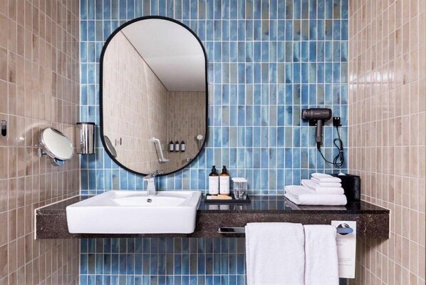 A bathroom with a white sink, a large mirror, a hairdryer, and neatly folded towels on a black countertop. - Mercure Ambassador Seoul Magok (Seoul)