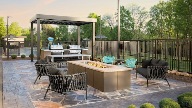 Une terrasse extérieure avec un sol en pierre, un barbecue, un foyer et des meubles en osier.
