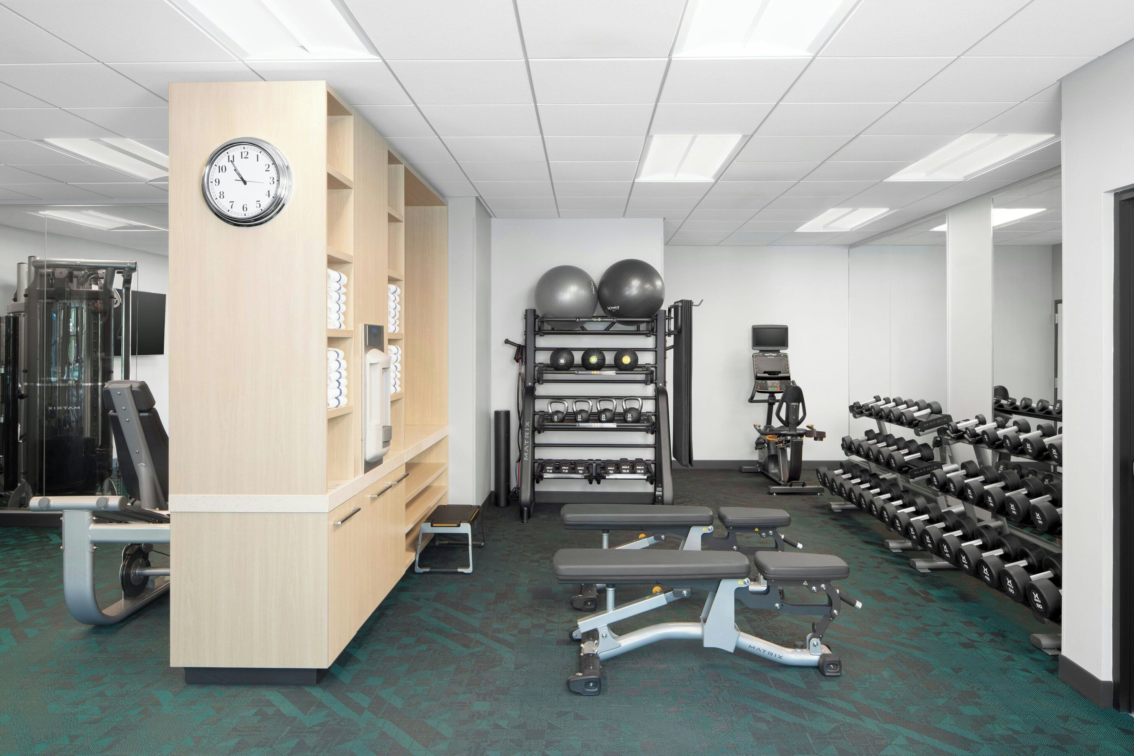 A gym with exercise equipment, a clock, and a wall-mounted shelf.