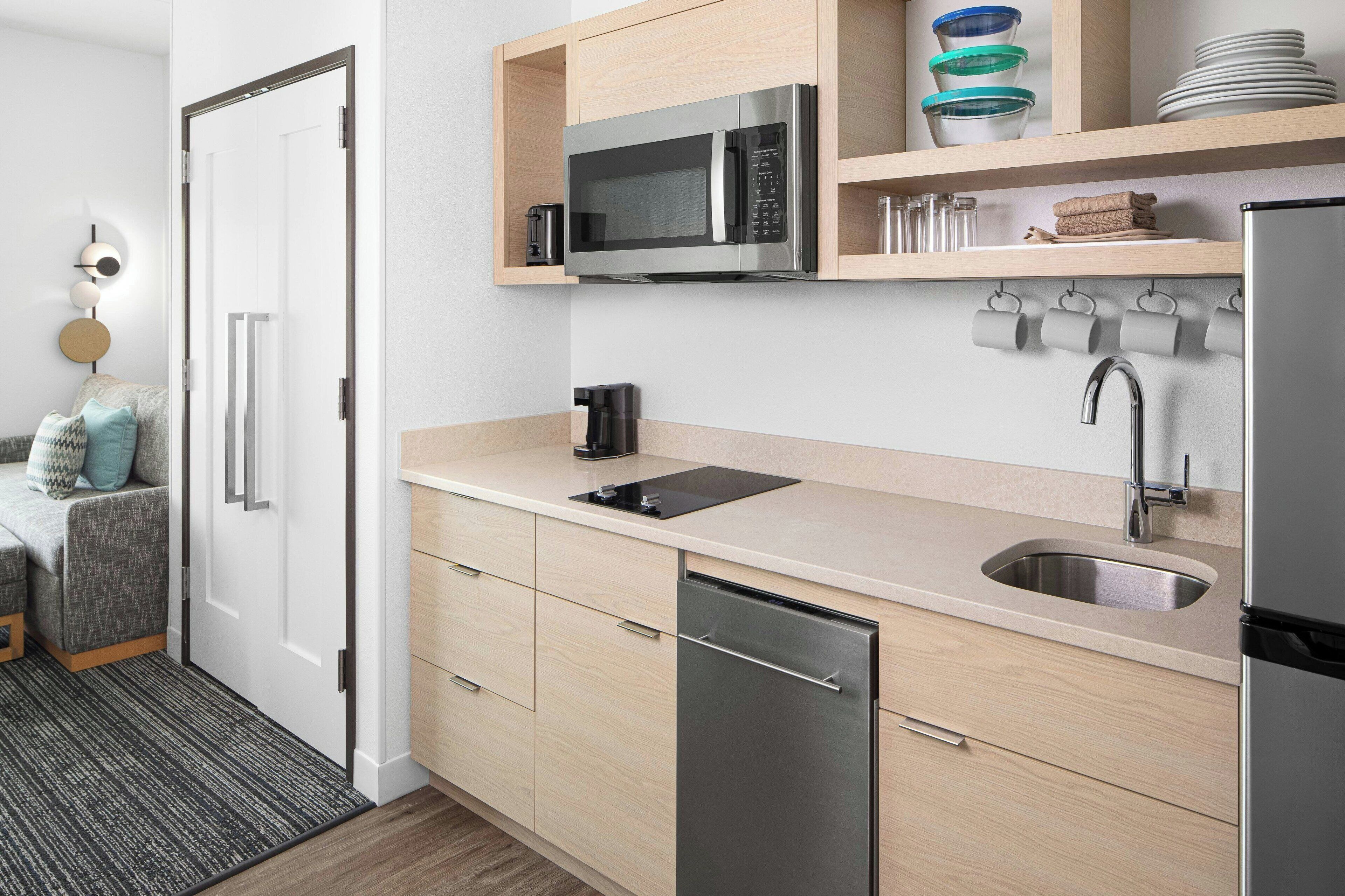 Een moderne keuken met een inbouwmagnetron, een spoelbak en een vaatwasser. Houten keukenkastjes en een aanrechtblad zijn zichtbaar.