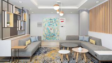 A modern lounge area with a sectional sofa, round tables, and a colorful abstract painting on the wall.