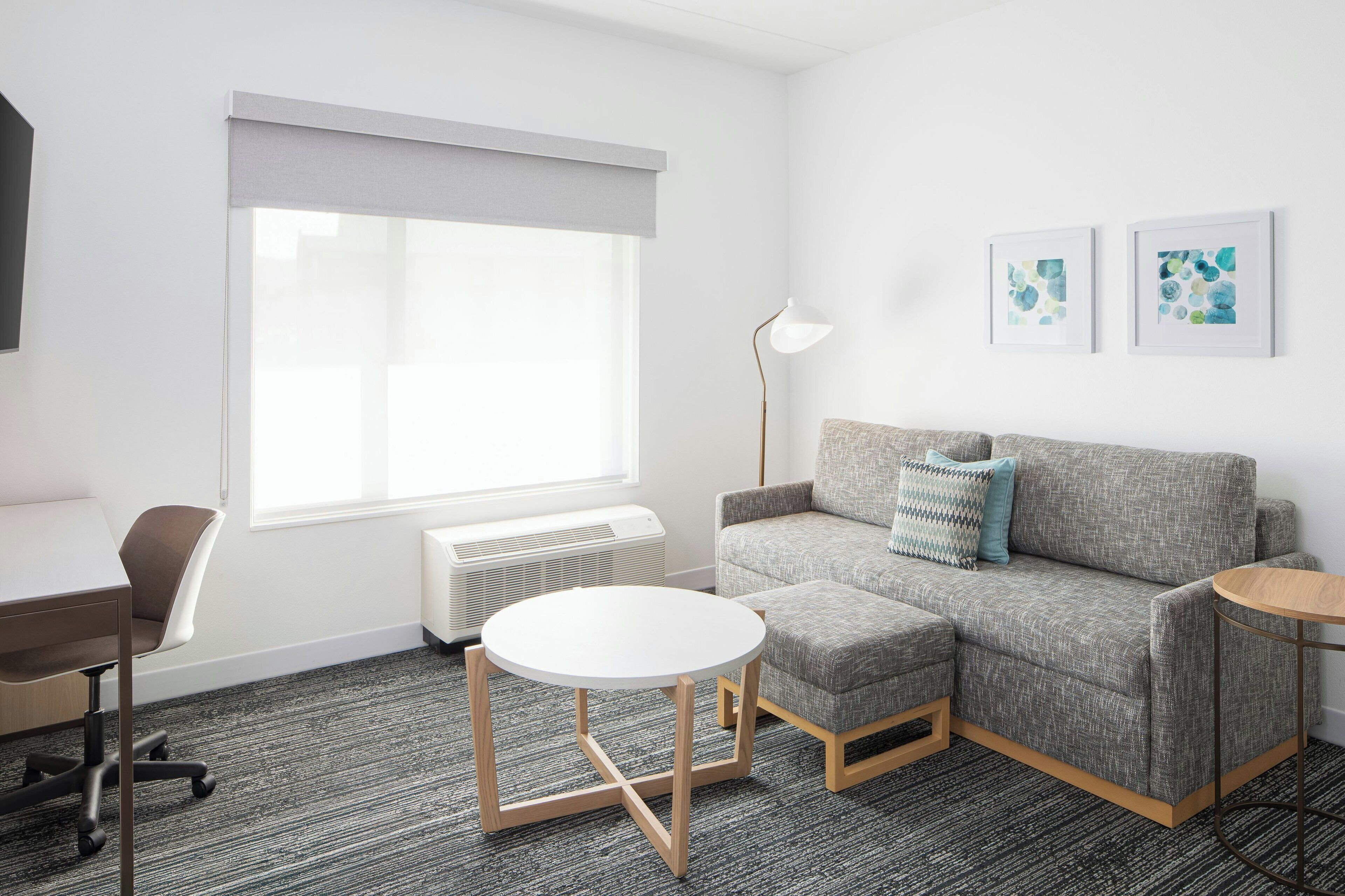 A modern room with a grey sofa, a round white table, a grey armchair, and a standing lamp.