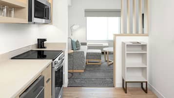 A modern kitchen with built-in appliances, a dining area with a sofa and table, and a small bookshelf.