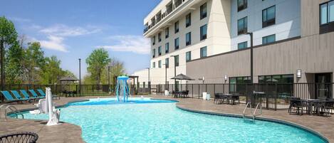 A hotel with a swimming pool, lounge chairs, and a covered seating area.