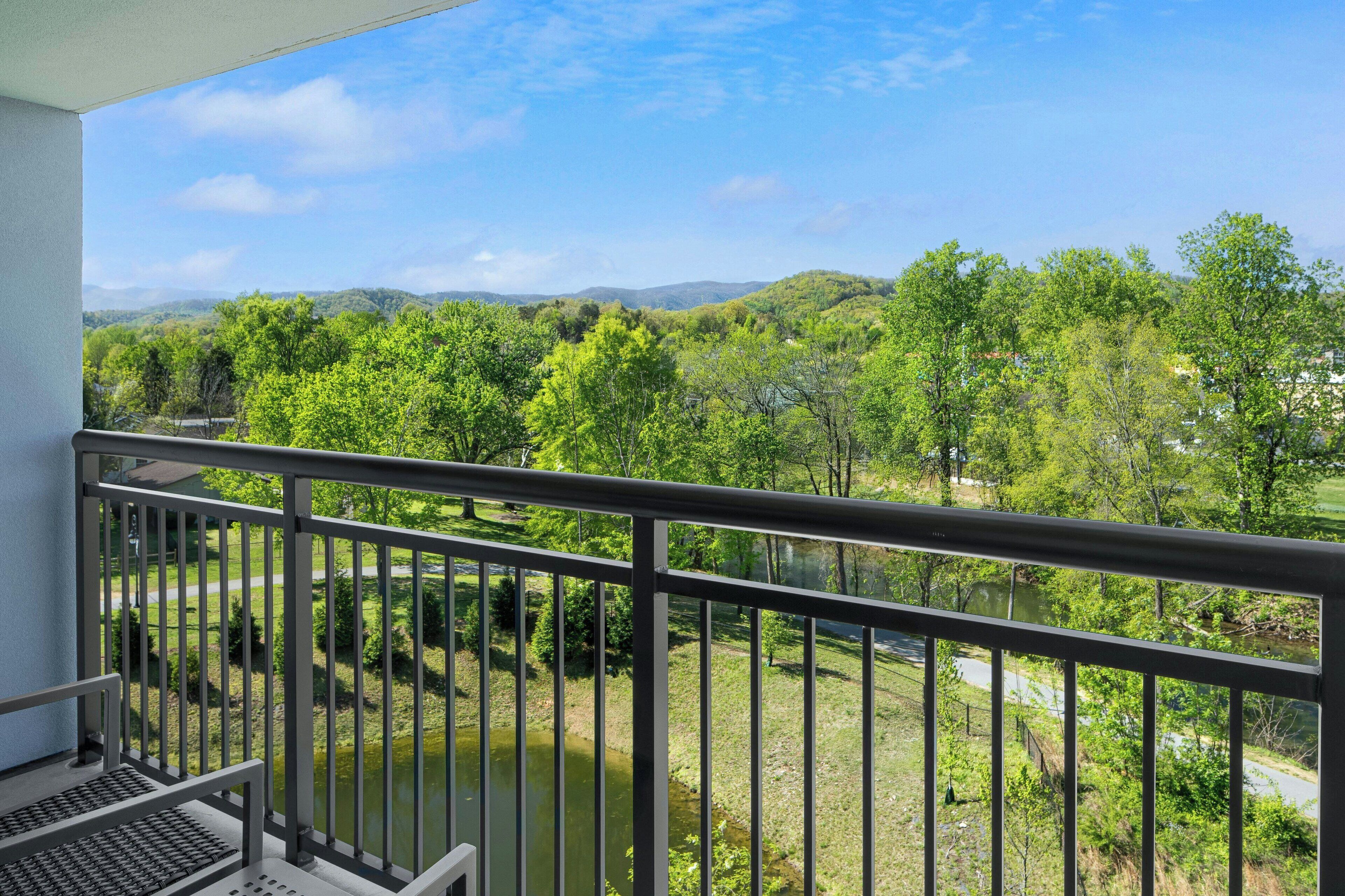 A balcony with a view of a river and surrounding greenery.