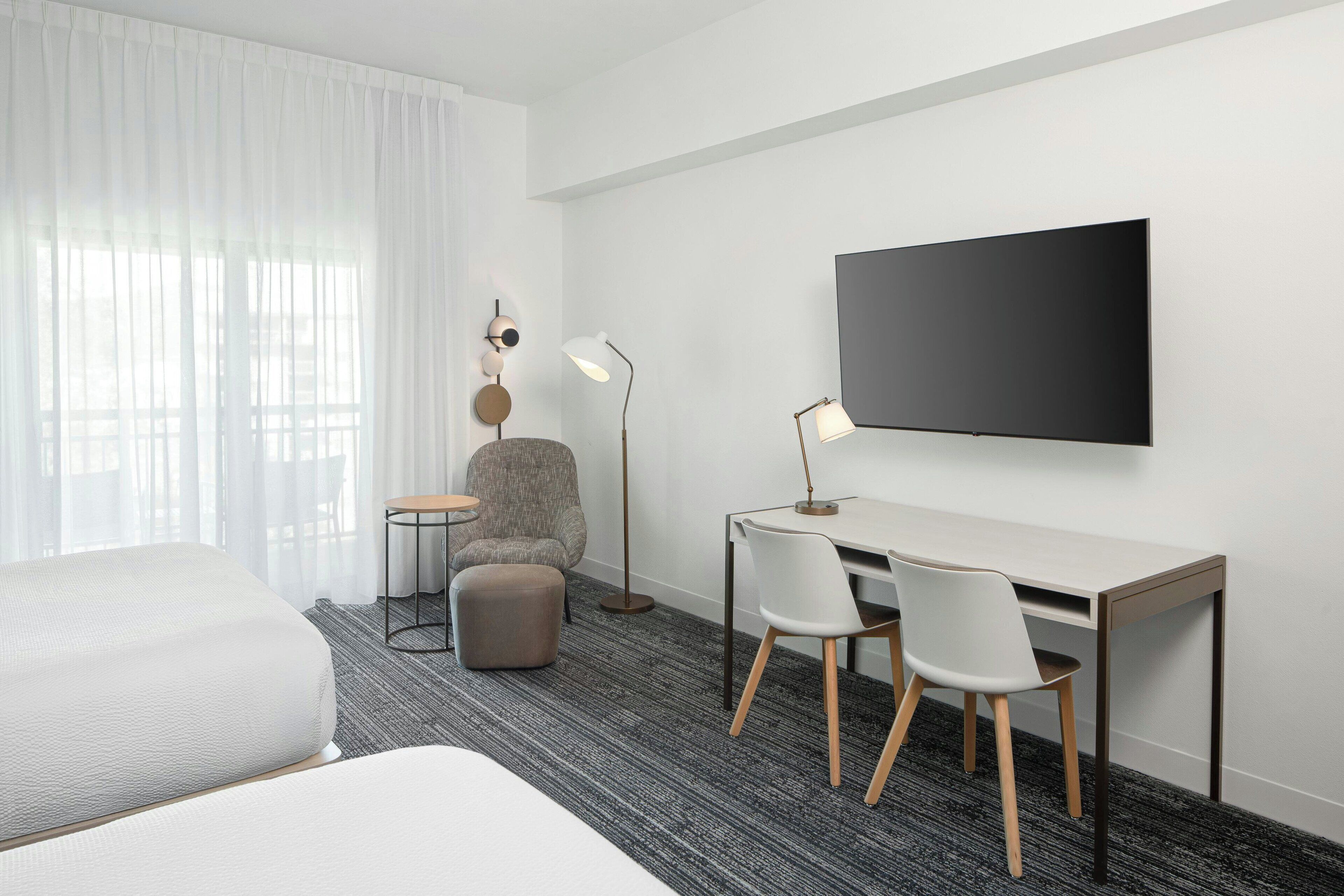 A hotel room with a bed, a desk with two chairs, a television, and a lamp.