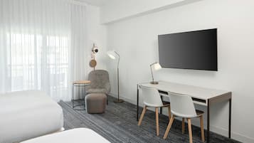 A hotel room with a bed, a desk with two chairs, a television, and a lamp.