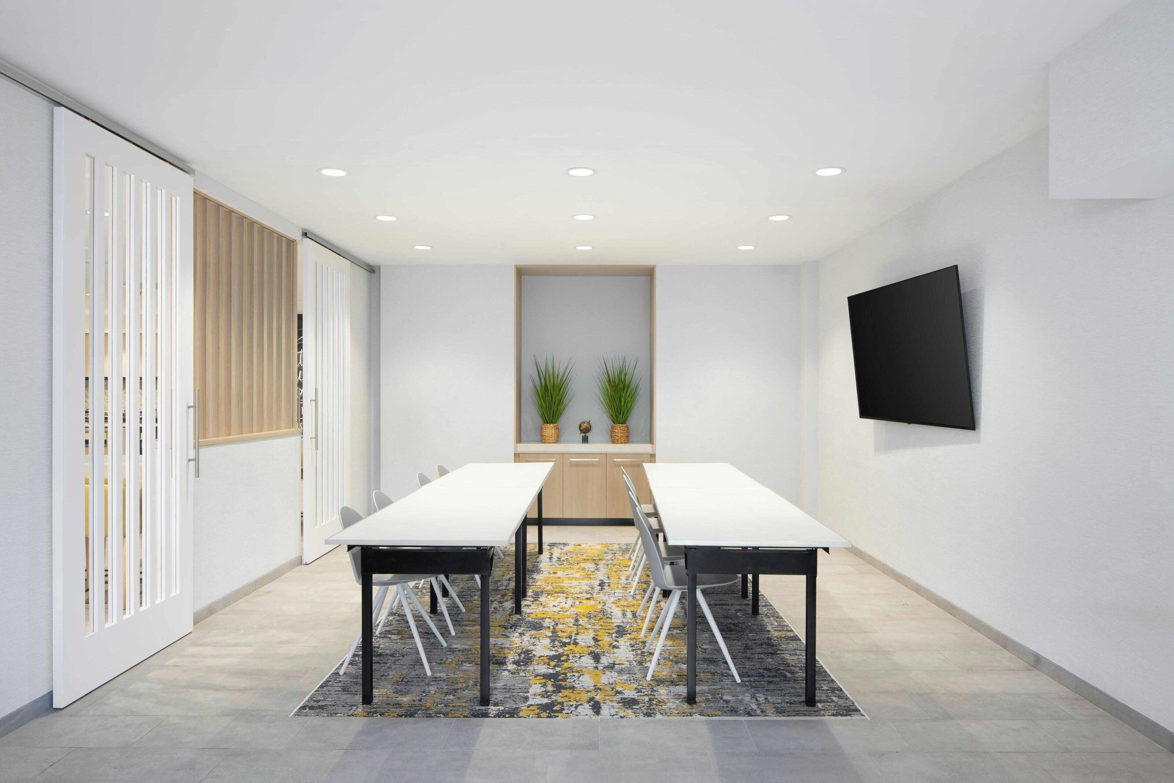 A conference room with a long table, chairs, a TV, and plants.