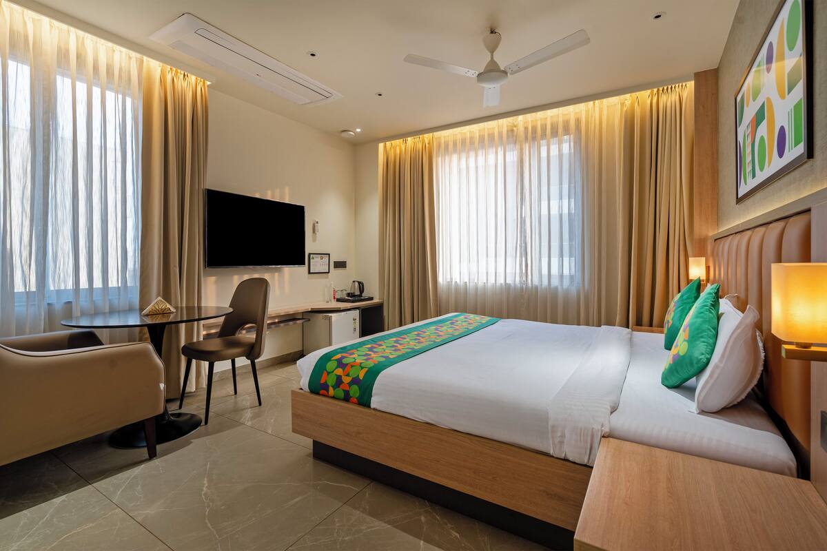 Una habitación de hotel con una cama, un escritorio con silla, televisión y ventilador de techo.