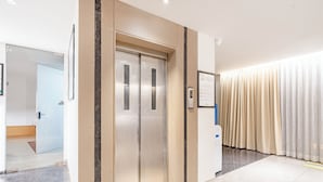 A modern elevator with metallic doors, a wall-mounted sign, and a curtain to the right. - Treebo Premium Lalitha, RK Beach (Visakhapatnam)