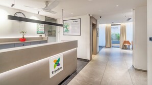 A modern reception area with a reception desk labeled "treebo," a clock, and a framed informational poster. - Treebo Premium Lalitha, RK Beach (Visakhapatnam)