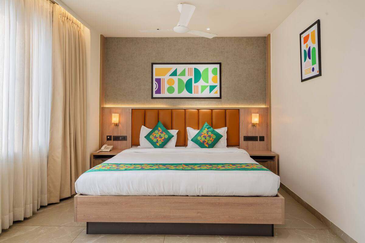 Una habitación de hotel moderna con una cama grande, cabecero de madera y dos mesitas de noche con lámparas.