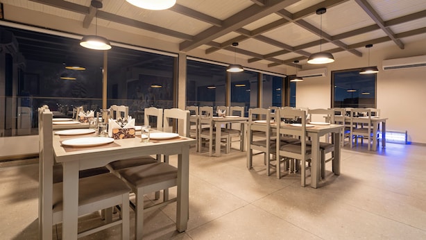 A dining area with multiple tables and chairs, large windows, and pendant lighting. - Treebo Premium Lalitha, RK Beach (Visakhapatnam)
