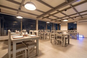 A dining area with multiple tables and chairs, large windows, and pendant lighting. - Treebo Premium Lalitha, RK Beach (Visakhapatnam)