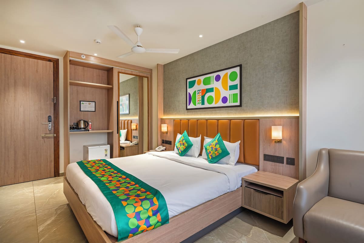 Habitación de hotel moderna con una cama grande, un escritorio, una silla, un ventilador de techo y una obra de arte colgada en la pared.
