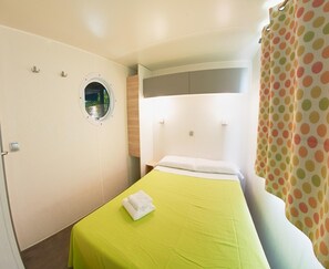 Una stanza piccola con un letto singolo, una finestra rotonda, una coperta verde e una tenda a pois.