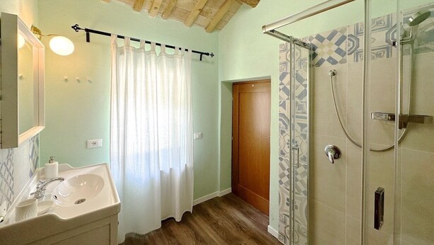 A bathroom with a wooden ceiling, a glass shower enclosure, a sink with a mirror, and a door leading to another room. - Historic House With Swimming Pool, Barbecue, gym in Senigallia - The Quercia (Senigallia)