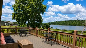 A deck with outdoor furniture, a view of a lake, and a forested area in the background. - Waterfront Cabin | Near ARK | Large Family Retreat (Warsaw)