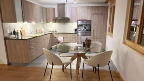 A modern kitchen with wooden cabinets, a built-in oven, and a glass dining table with four chairs. - Contemporary Swiss Escape (Gsteig)
