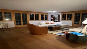 A spacious living room with a brown leather sofa, a white sofa with striped pillows, and a coffee table. There is a bookshelf and a lamp in the room. - Contemporary Swiss Escape (Gsteig)
