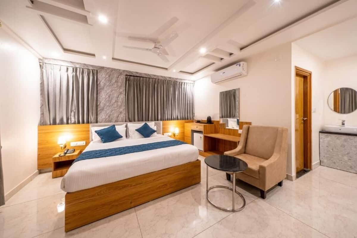 A modern hotel room with a wooden bed, a round table, a sofa, and a bathroom with a sink and mirror.