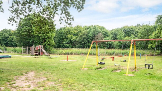 A playground with swings and a slide, surrounded by grass and trees. - 4 Person Holiday Park Home in Jelling (Jelling)