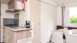 A compact kitchen with a gas stove, coffee maker, and a small dining area with a table and chairs. - 4 Person Holiday Park Home in Jelling (Jelling)