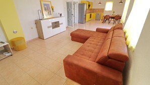 A modern living room with a large sectional sofa, a kitchen with yellow cabinets, and a dining area with a table and chairs.