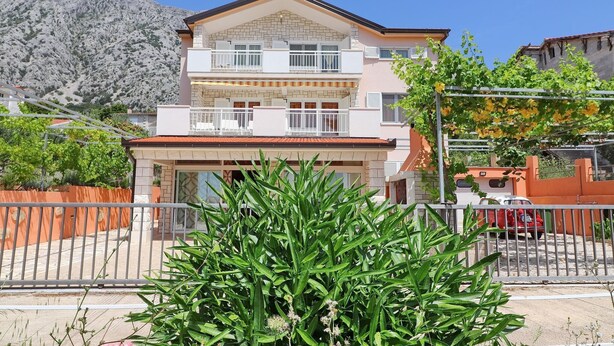A two-story building with a balcony, a garage, and a mountain backdrop.