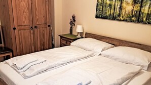 A double bed with white linens, a nightstand with a lamp, and a wooden wardrobe.