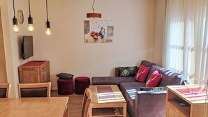 A modern living room with a wooden dining table, a sofa, and a TV mounted on the wall.