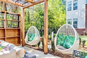 Eine Terrasse mit zwei Hängestühlen, einer Holzpergola und einem weißen Gebäude im Hintergrund.