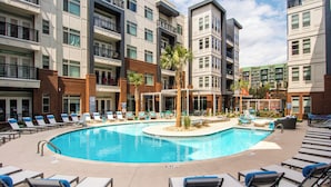 A swimming pool surrounded by lounge chairs and a multi-story building with balconies. - Ellison on Broad (Greenville)