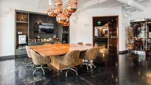 A modern conference room with a large wooden table, six upholstered chairs, and a large flat-screen TV on the wall. - Ellison on Broad (Greenville)