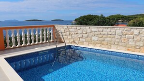 Une piscine bordée d’un mur en pierre et dotée d’un escalier en métal, offrant une vue sur une étendue d’eau et un paysage verdoyant.